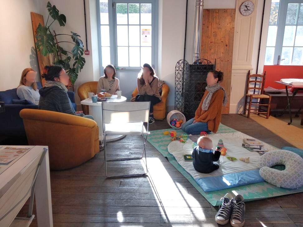 Un groupe de parents assis échangent sur leurs pratiques. un bébé joue sur un tapis.