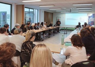 une salle de réunion, un personnes fait une présentation à des personnes assises autour de la table