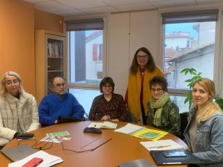 Des personnes assises autour d'une table, un personne debout au fond.